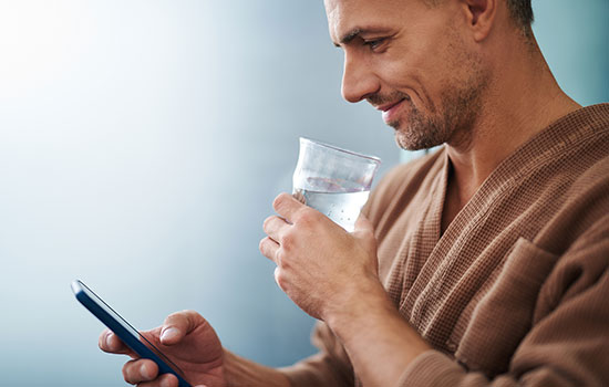man looking down at smartphone while holding a glass of water