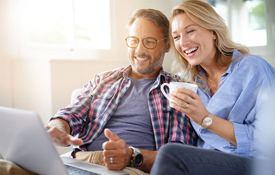 smiling, mature couple using laptop while drinking coffee