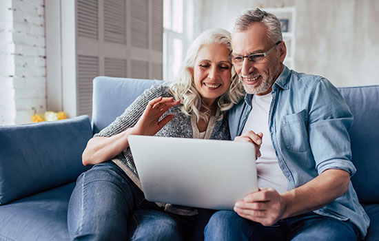 two smiling seniors on a couch using a laptop