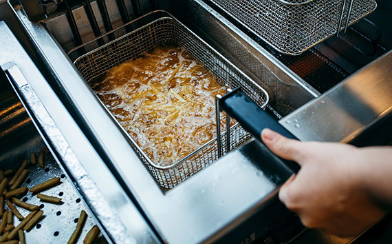 over the shoulder view of a person frying french fries in grease in a restaurant kitchen