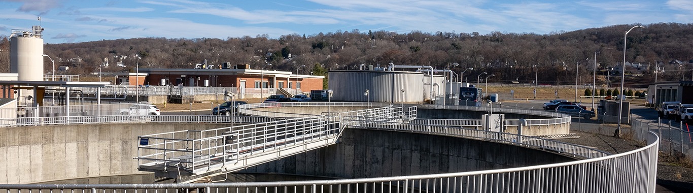 Aerial view of a wastewater treatment facility with circular clarifier tanks and a brick operations building.