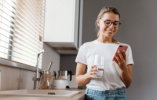 young woman holding glass of water while dialing phone